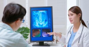 A female doctor explained x-ray film on the computer to a male patient at the clinic. The patient is asking the doctor, What to do if you experience colon pain over time?”